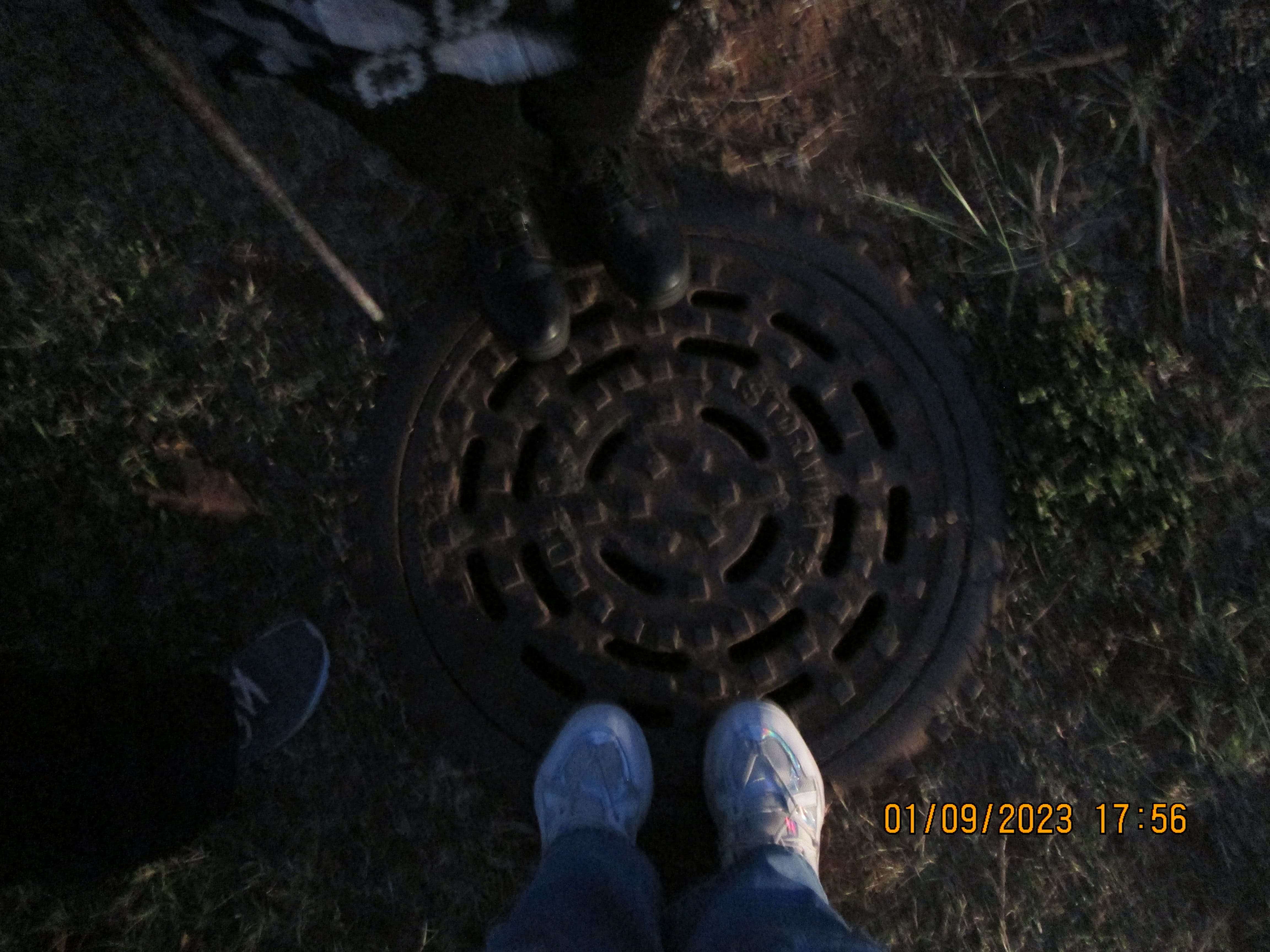 topdown view of shoes and there owners on a manhole cover, there is a light coming from somewhere outside the picture